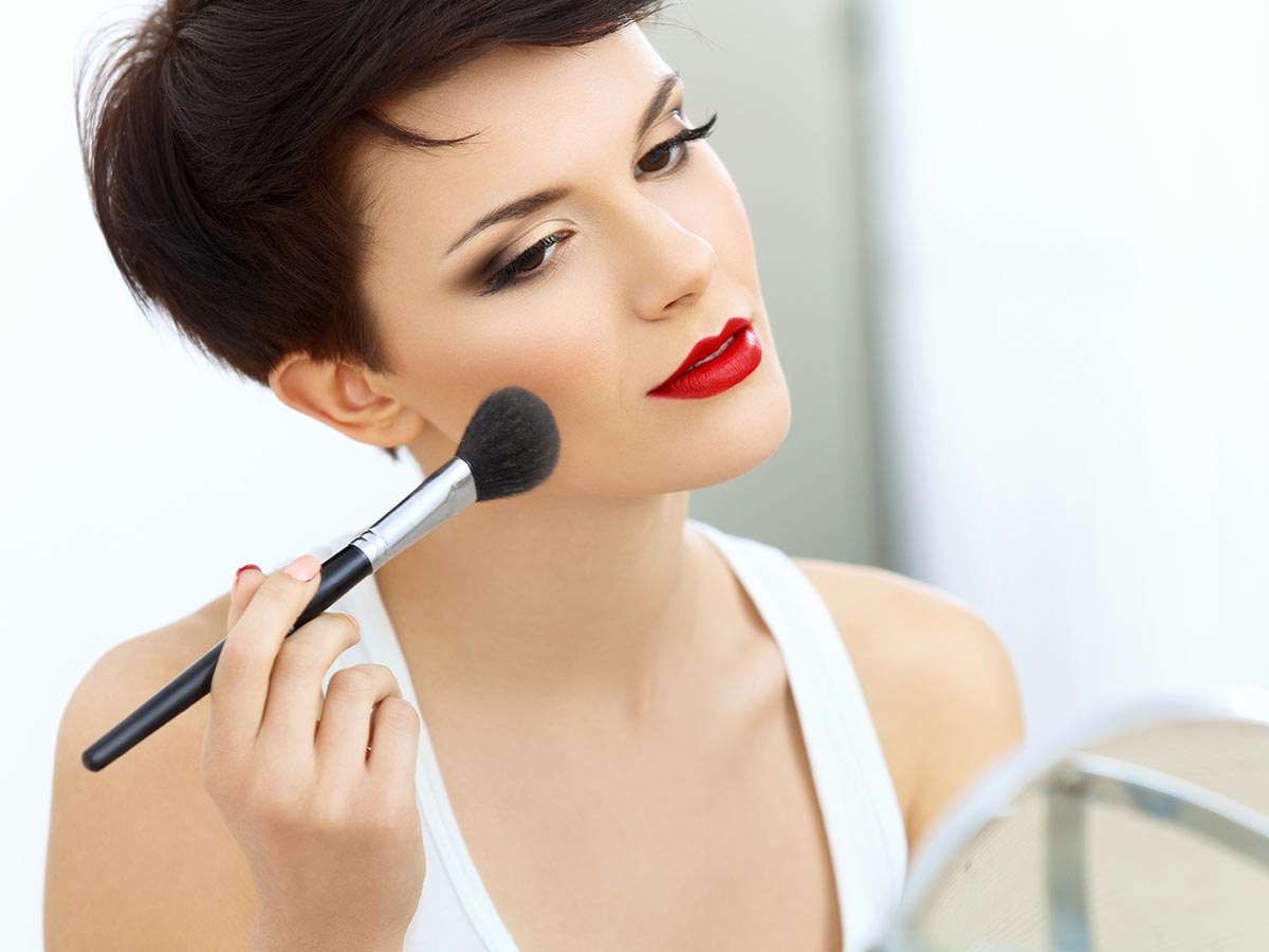 Brunette woman applying blush to her cheek