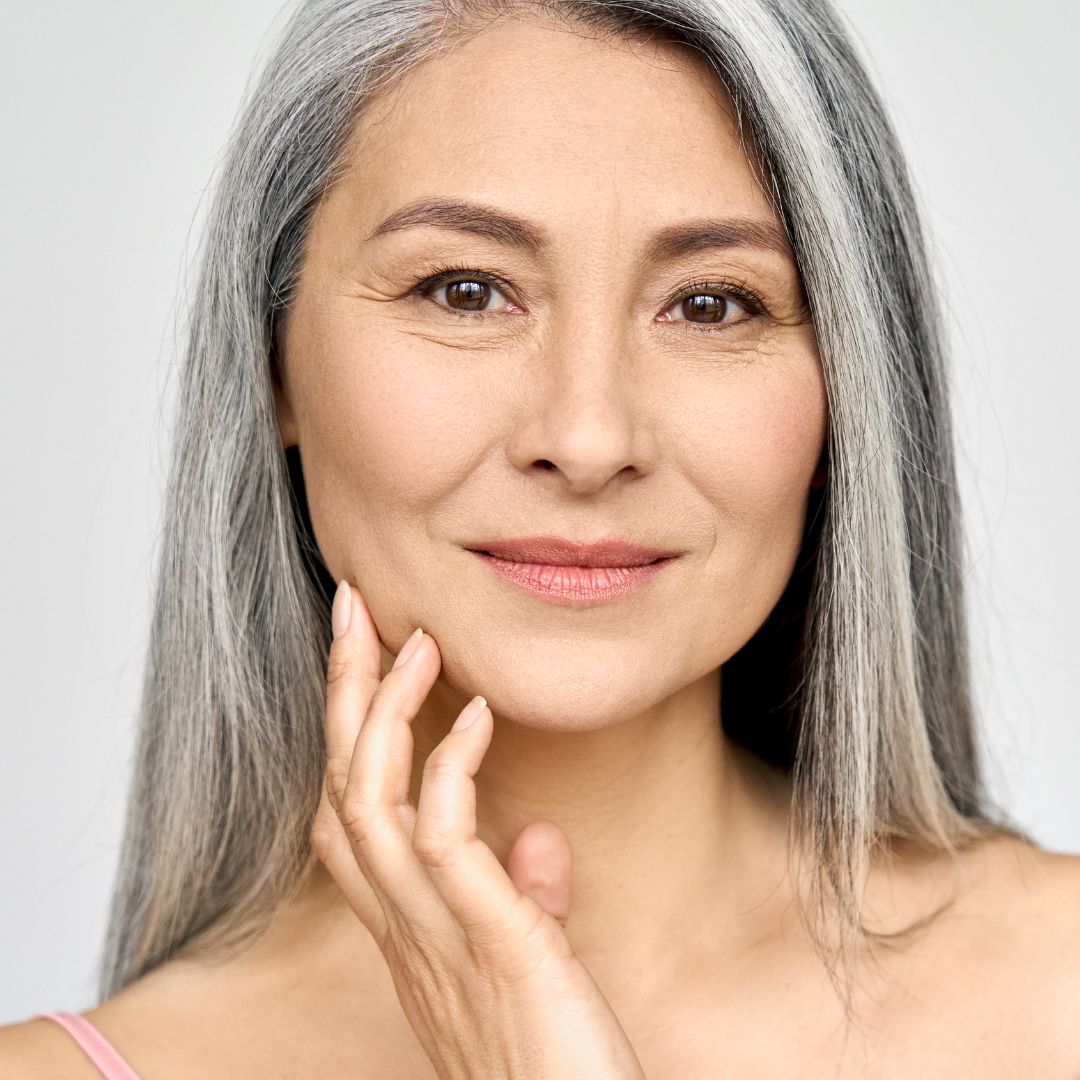 Woman with gray hair touching her face and smiling softly. 